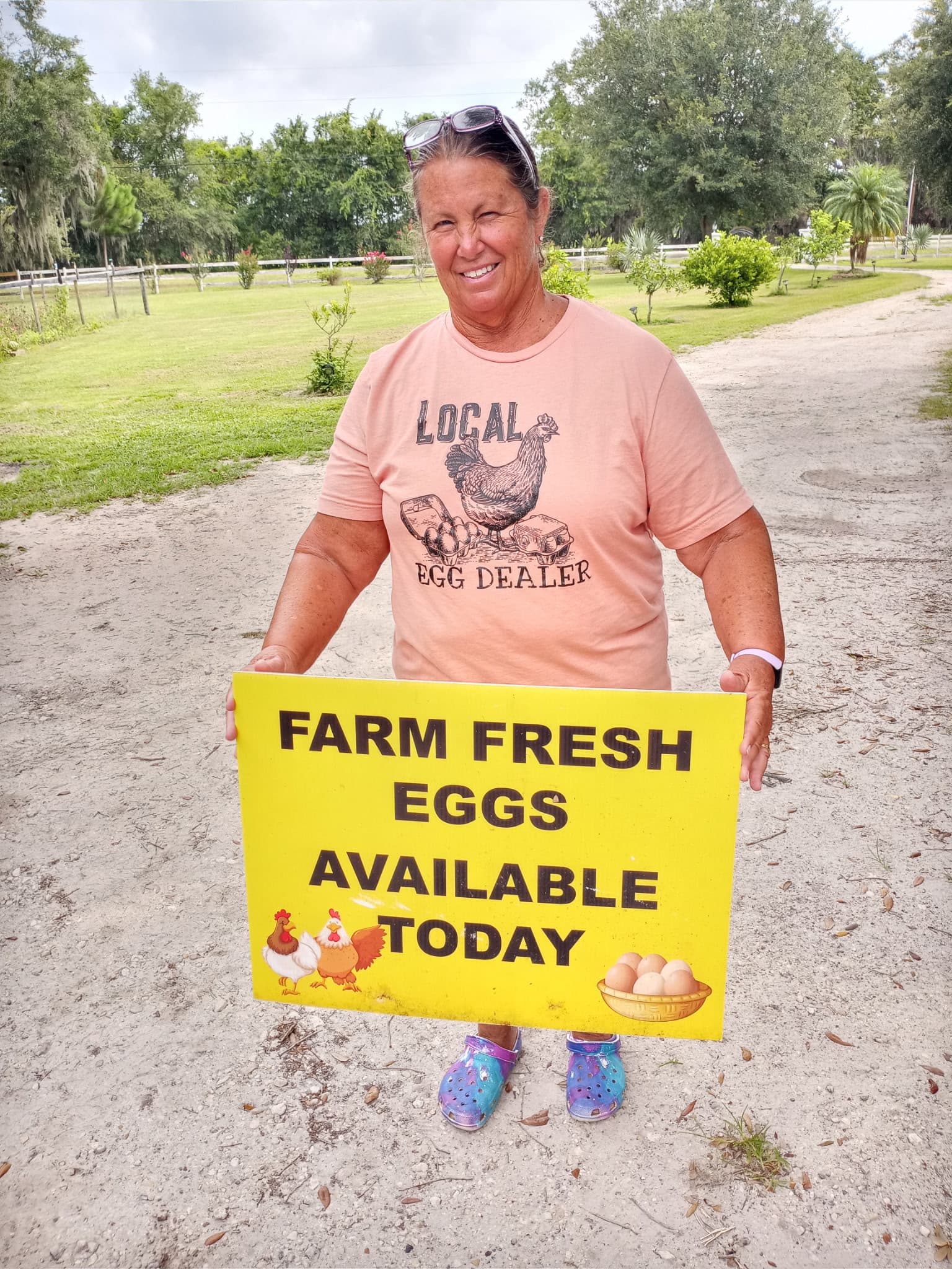 Sandi standing on the farm drive holding her Farm Fresh Eggs Available Today sign